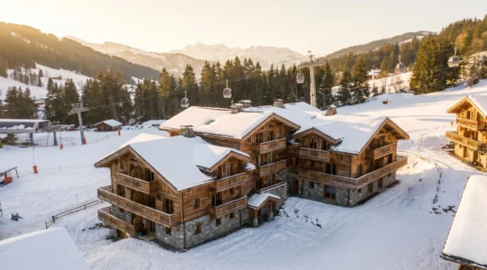 Vue extérieure d'un immeuble de studios aux Gets avec les remontées mécaniques visibles en arrière-plan, enneigé en hiver